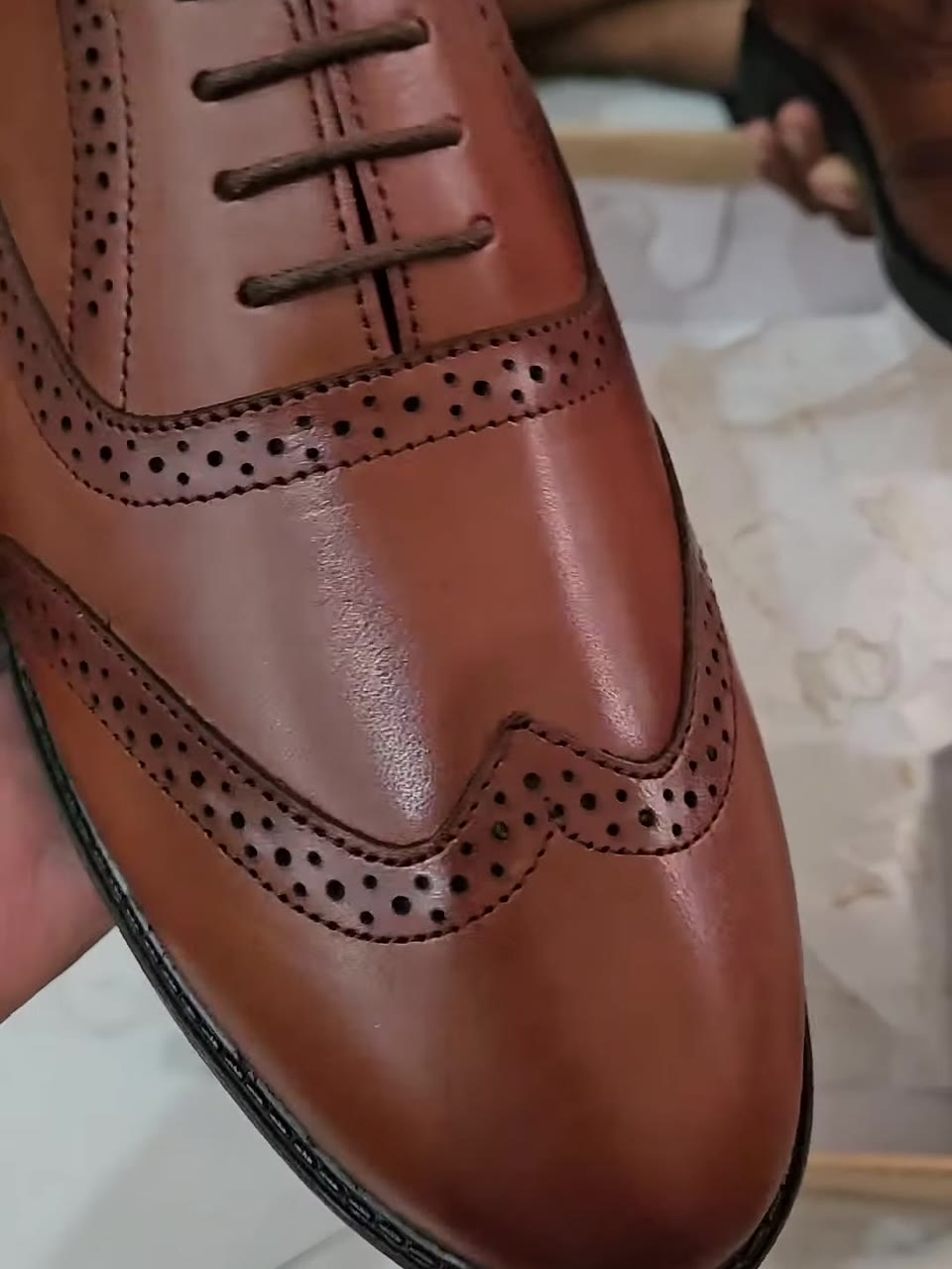 Tan crust leather wingtip brogue held in hand, showing the brogue perforation and stitching
